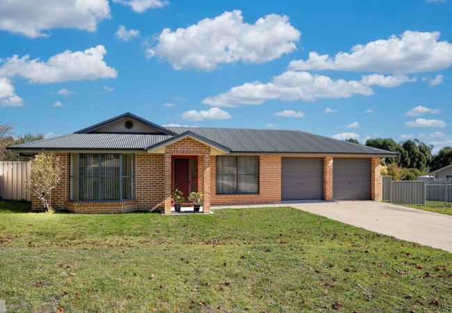 Brick house with a dark gray roof, two-car garage, and green lawn under a blue sky with clouds.