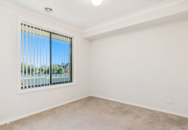 Empty room with a window, vertical blinds, and beige carpet. Bright sunlight streams in.
