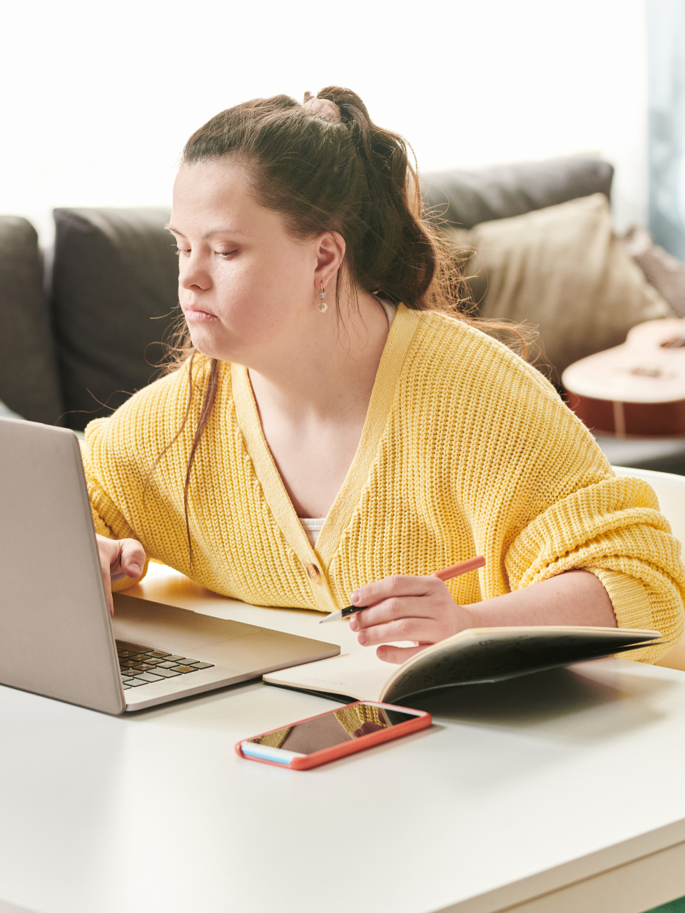 Man in a wheelchair using a laptop at a wooden table in a kitchen. He is smiling and wearing a blue shirt.