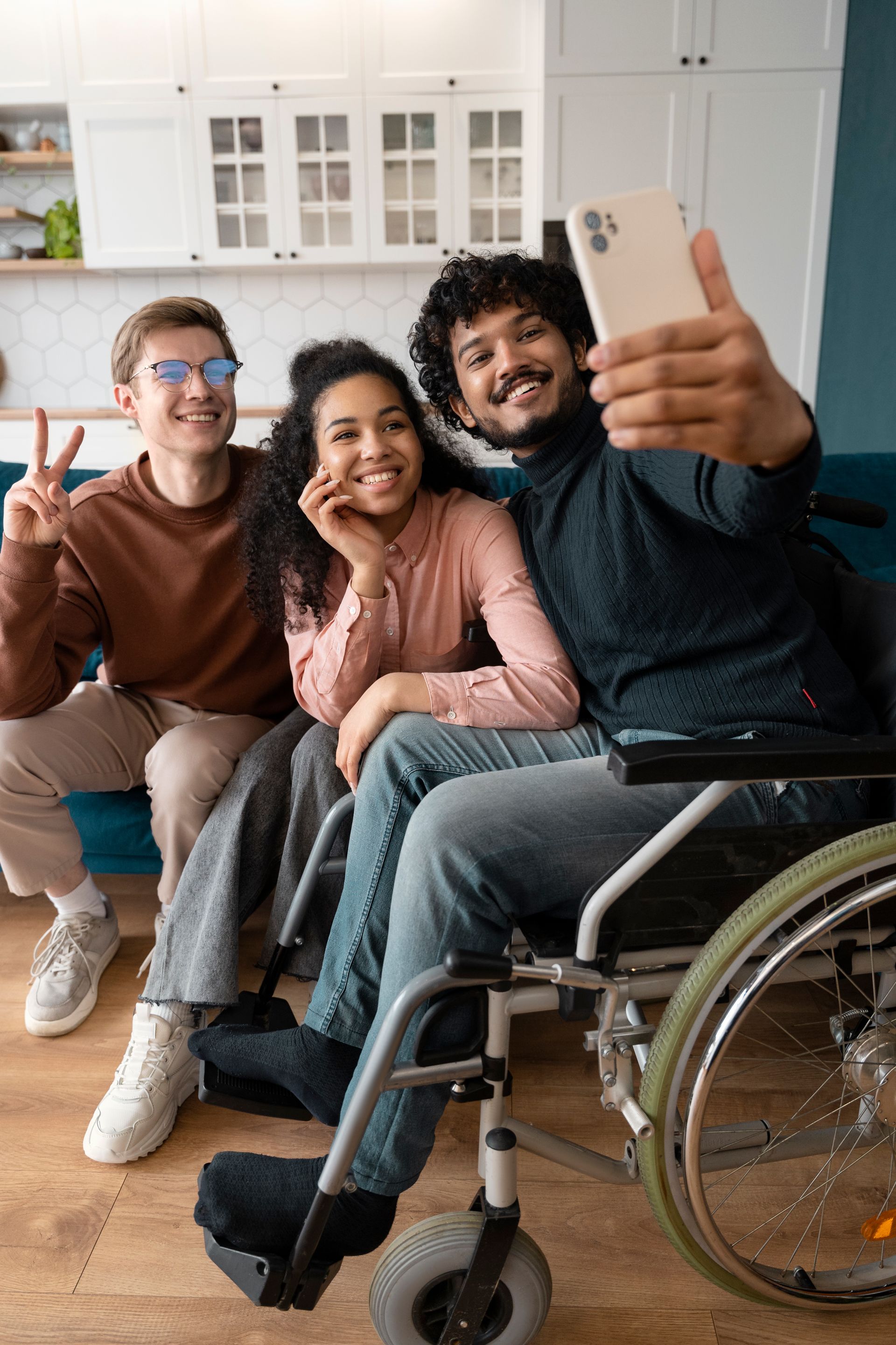 Three diverse friends taking a selfie: one in a wheelchair, one giving the peace sign, and one smiling.
