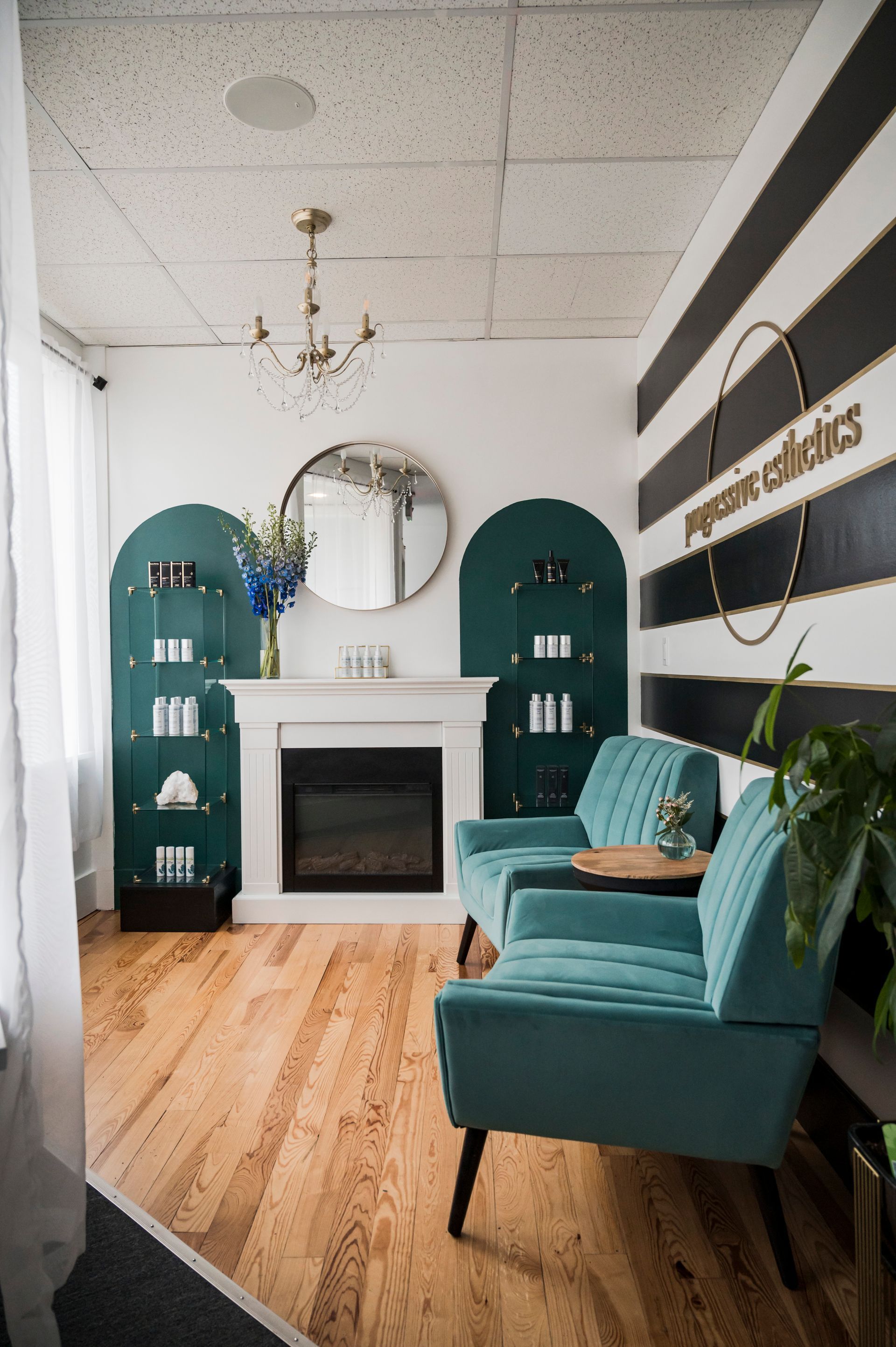 Waiting room with teal sofas, fireplace, and green shelves; black and white striped wall.