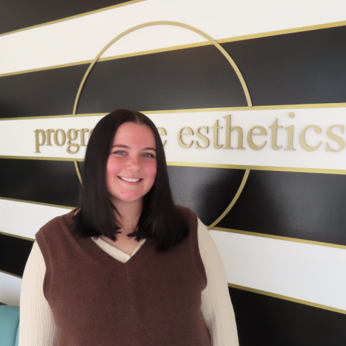 Woman with dark hair smiles in front of a sign that says