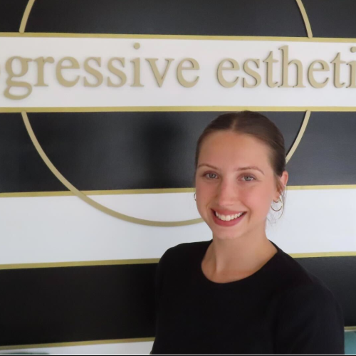 Woman with long brown hair, wearing a white shirt and hoop earrings, smiling in front of a black and white striped wall.