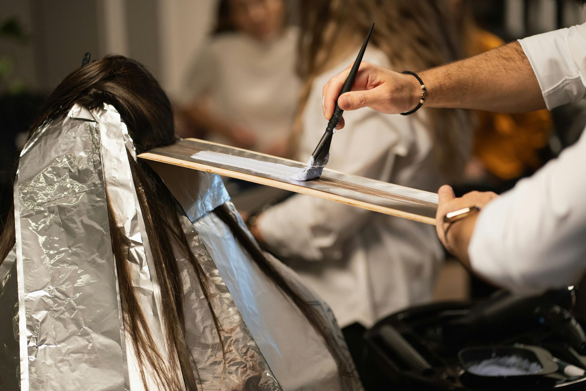 Hairdresser applying dye to hair with a brush, foil wrapped around sections, salon setting.