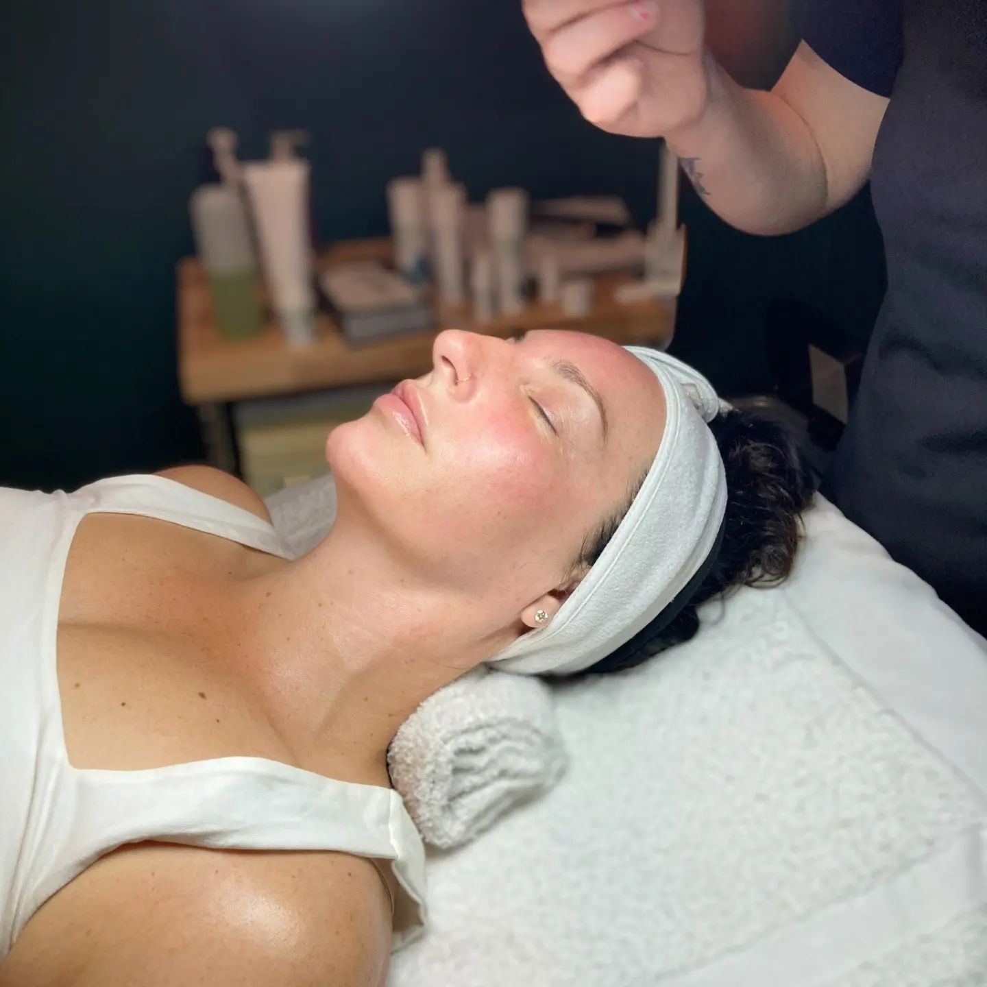 Hair stylist spraying hair with hairspray; woman's hair in an updo; another woman in background.