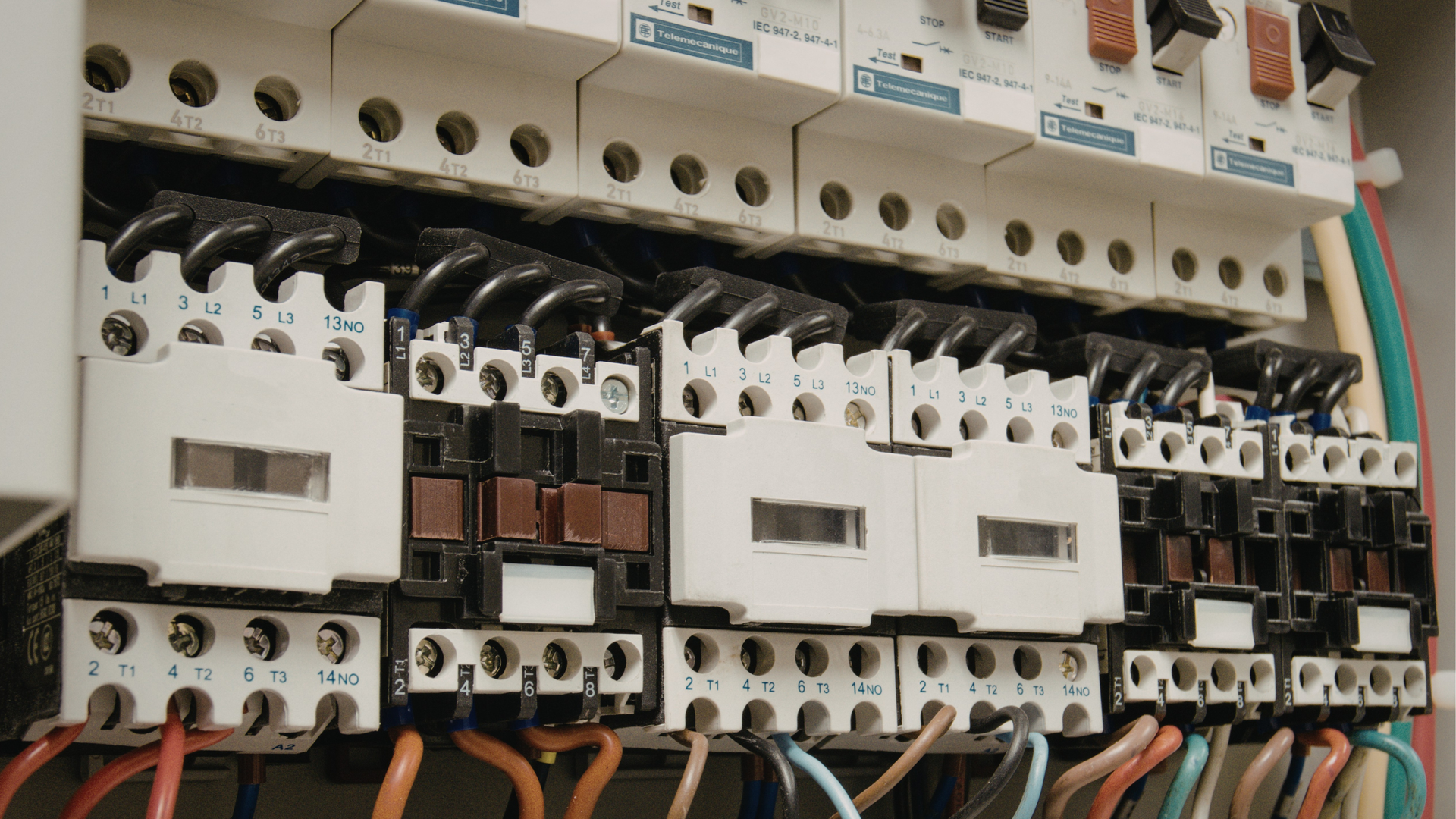 Close-up view of an electrical panel featuring several white contactors and circuit breakers with wired connections.