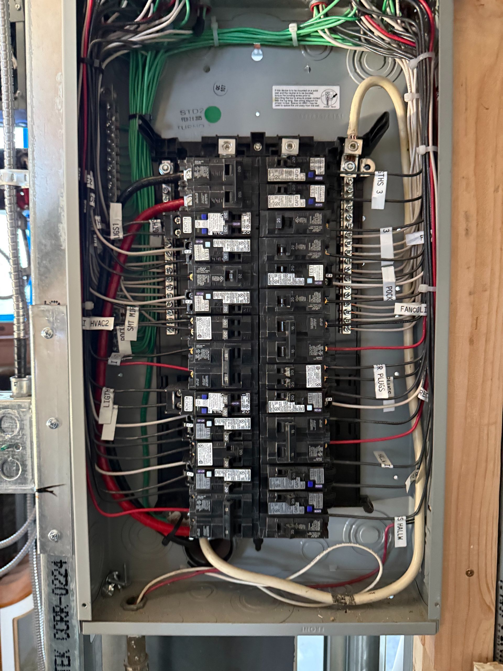 Three electrical panels with exposed colorful wiring and circuit breakers mounted on an unfinished interior wall.