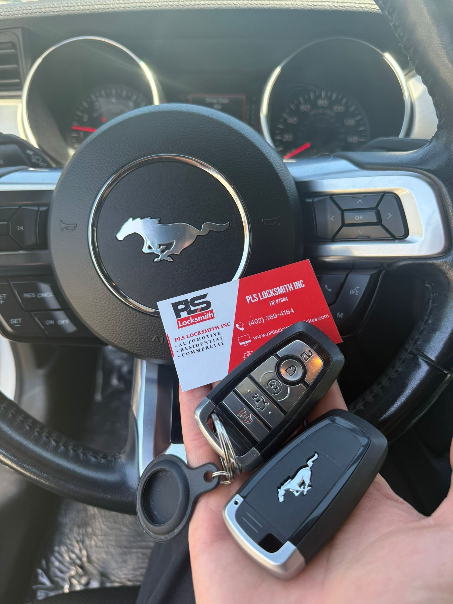 A person is holding two keys in front of a Mustang steering wheel.