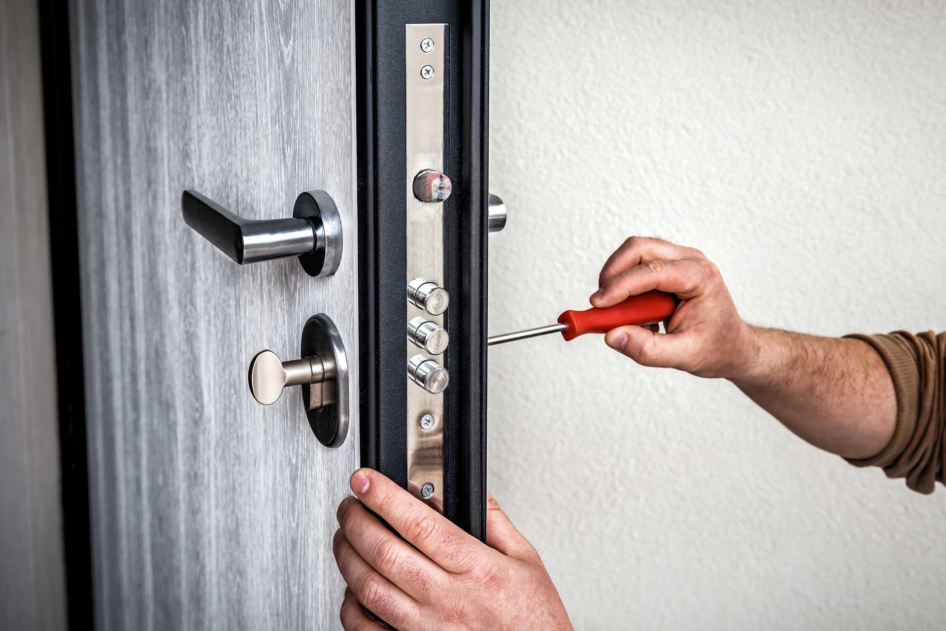 A person is fixing a door lock with a screwdriver.