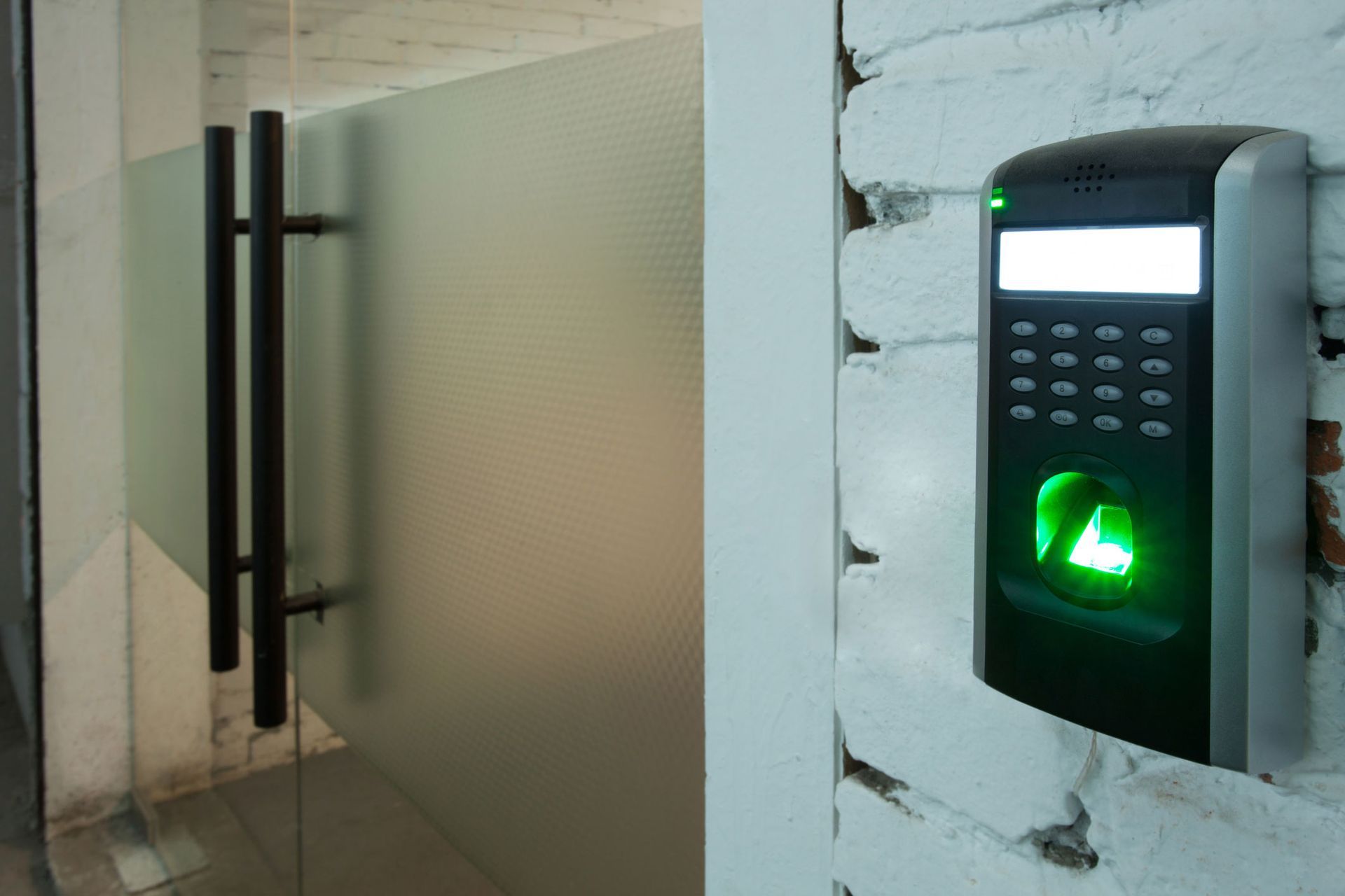 A fingerprint scanner is hanging on a brick wall next to a glass door.