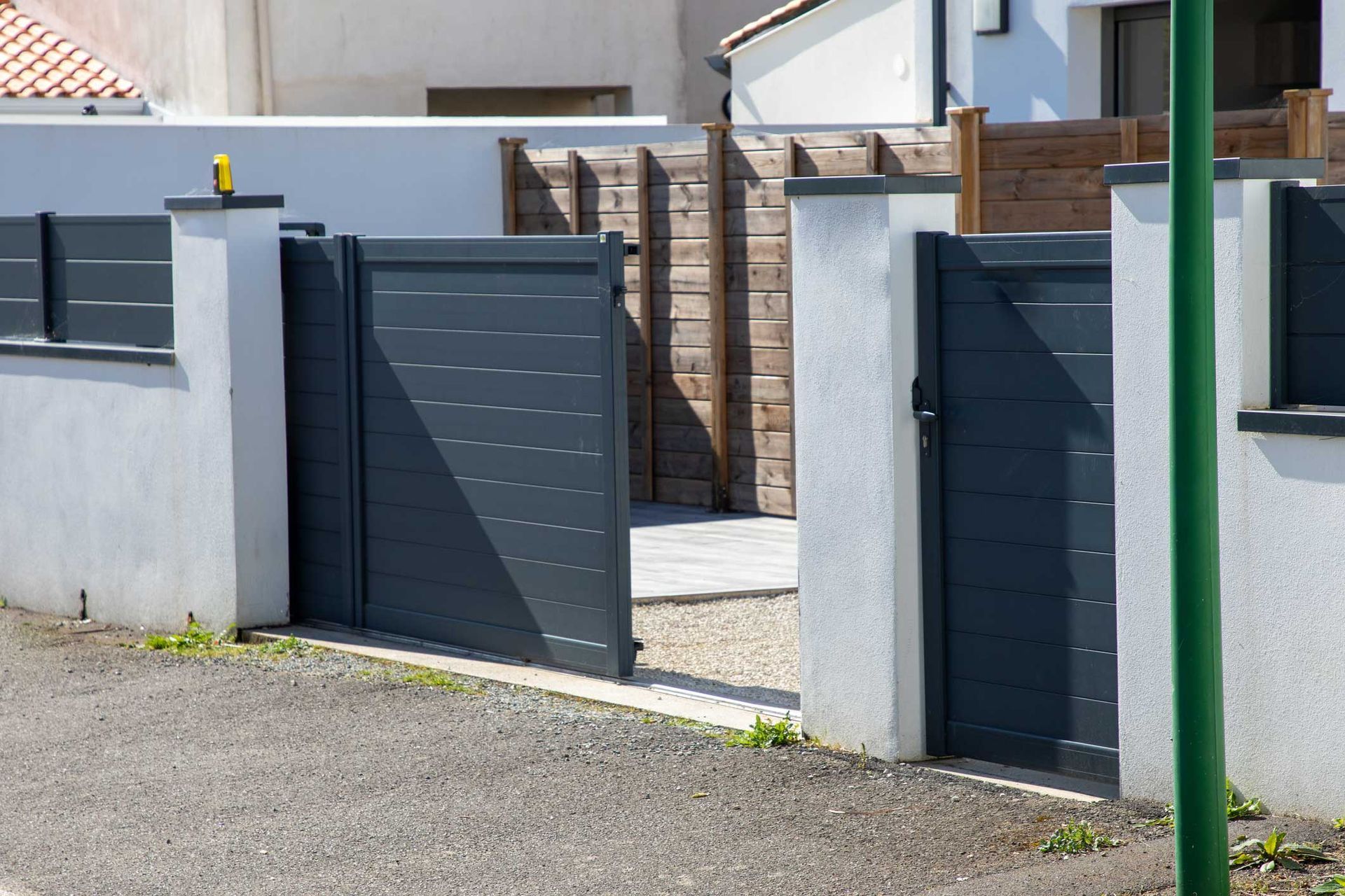 A black gate is open to a driveway in front of a house.