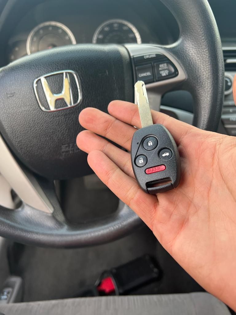 A person is holding a car key in front of a Honda steering wheel.