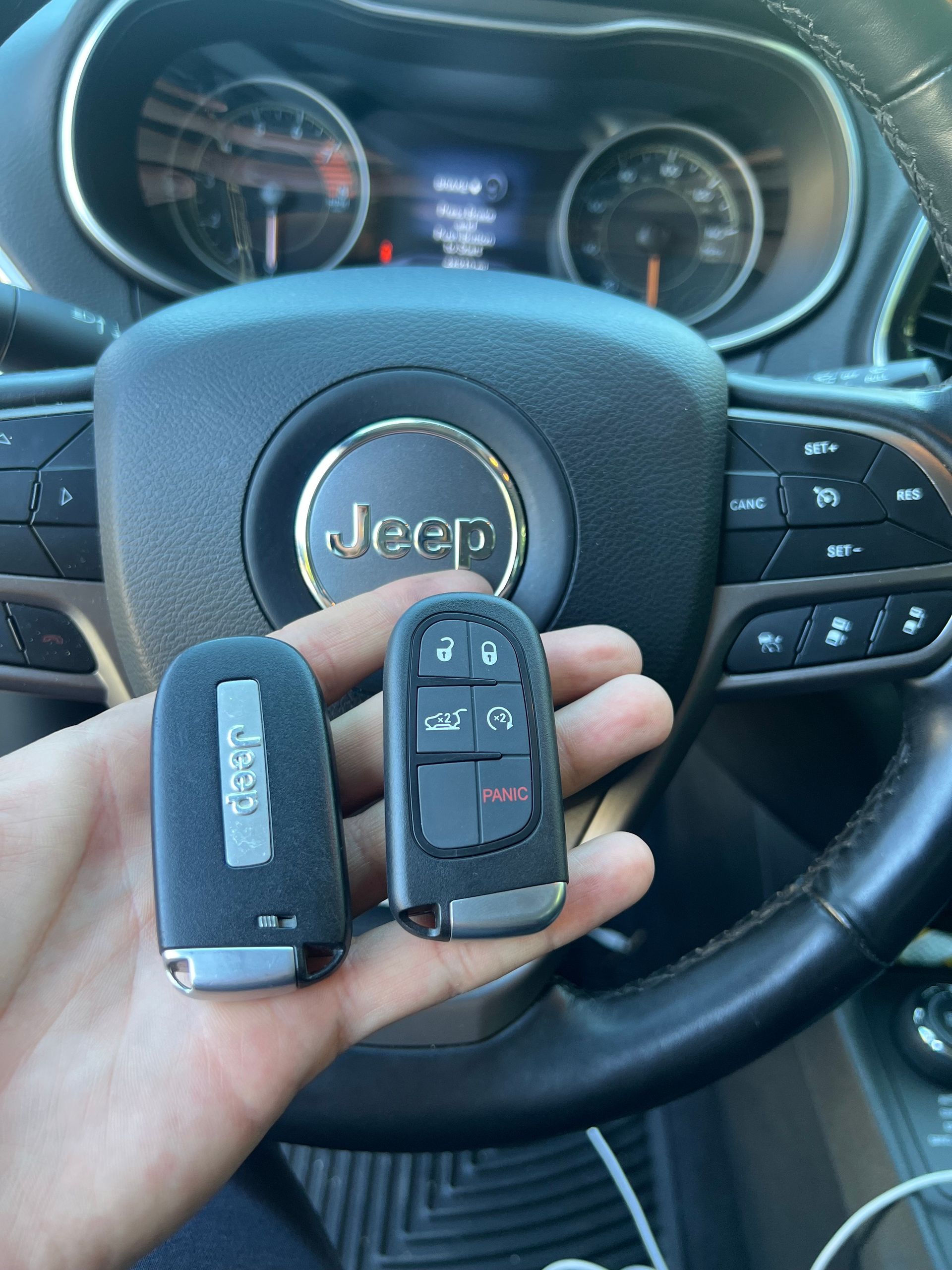 A person is holding two keys in front of a Jeep steering wheel
