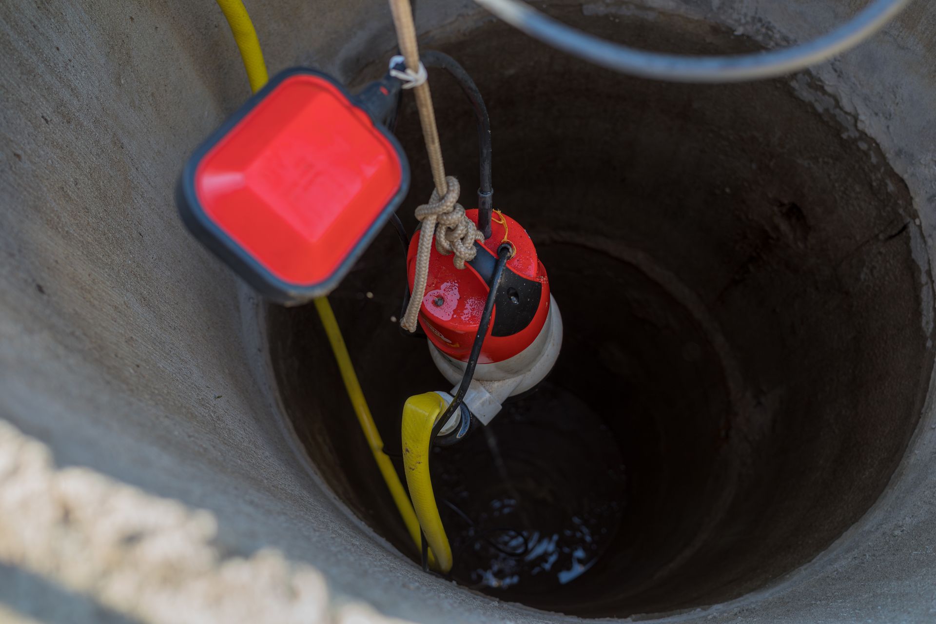 A red and black pump is sitting in a concrete well.