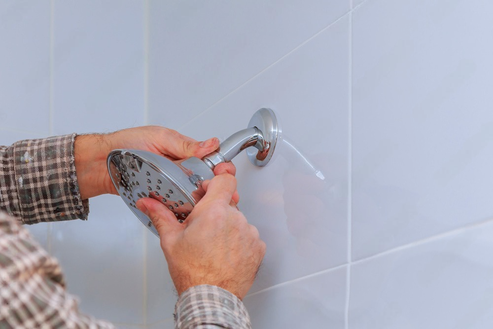 A man is fixing a shower head in a bathroom.