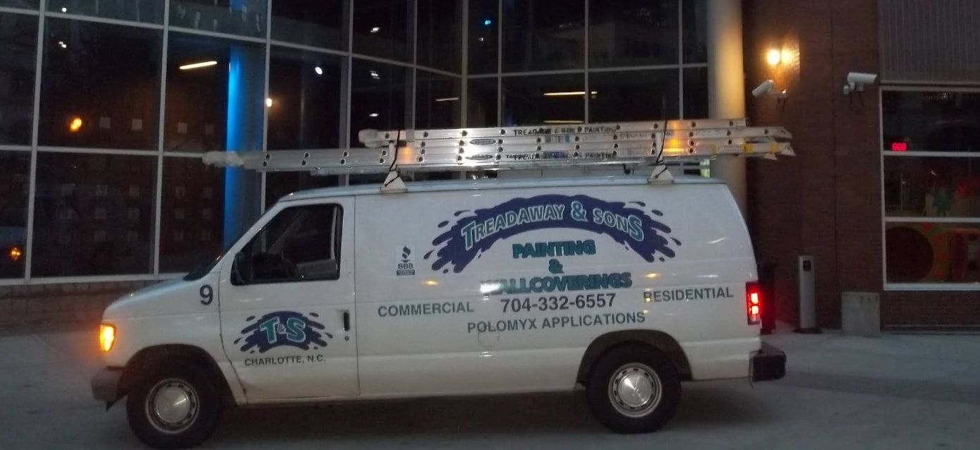 White van with ladder on top parked in front of a building at night.