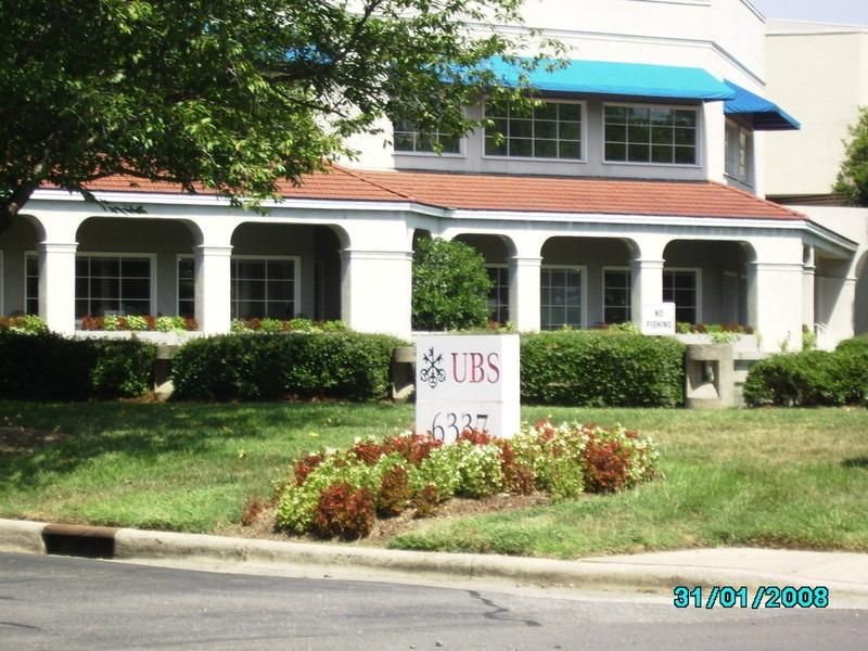 UBS sign in front of a white building with a red roof, blue awnings, and landscaped yard.