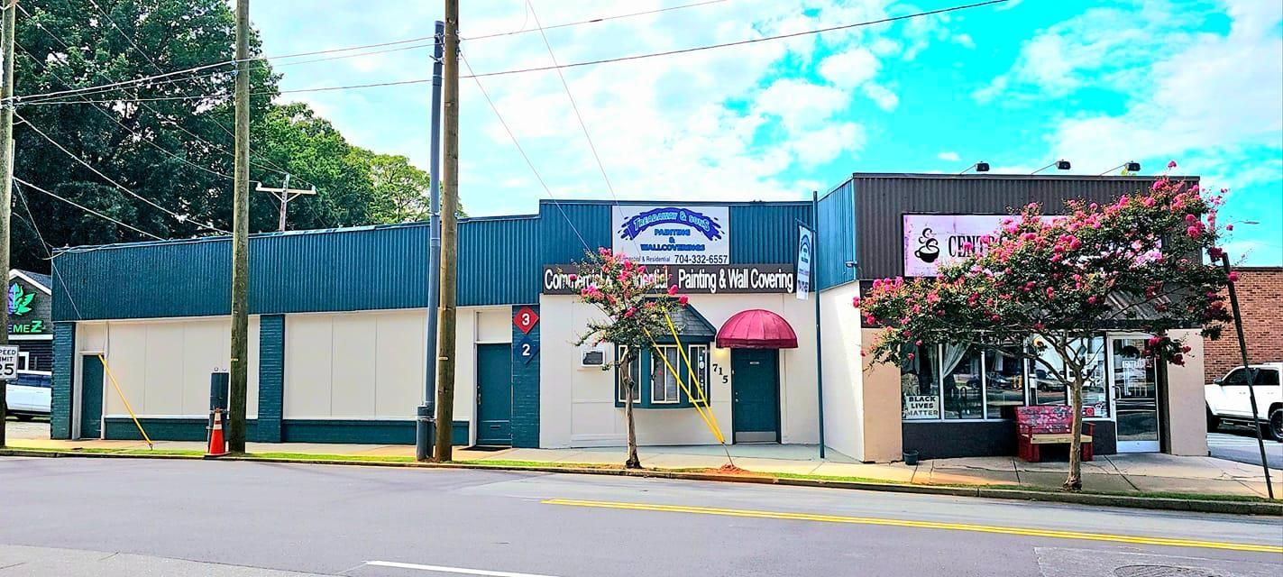Shops on a street with blue and gray buildings, green trees, and a cloudy sky.