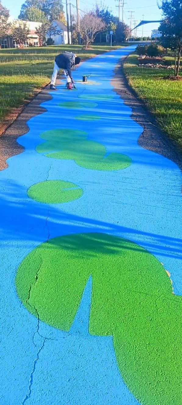 Person paints a blue river with green lily pads on a pathway in a residential area.