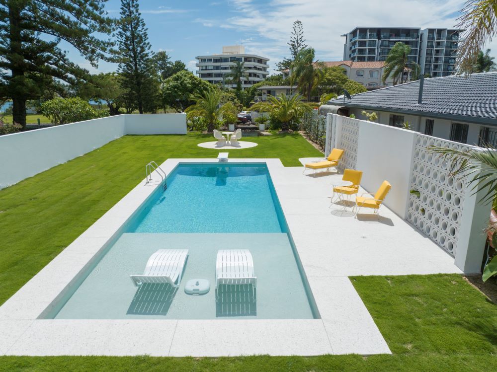 A Large Swimming Pool Surrounded by Chairs and Lawn — Beith Building & Developments Pty Ltd In Burleigh Heads, QLD