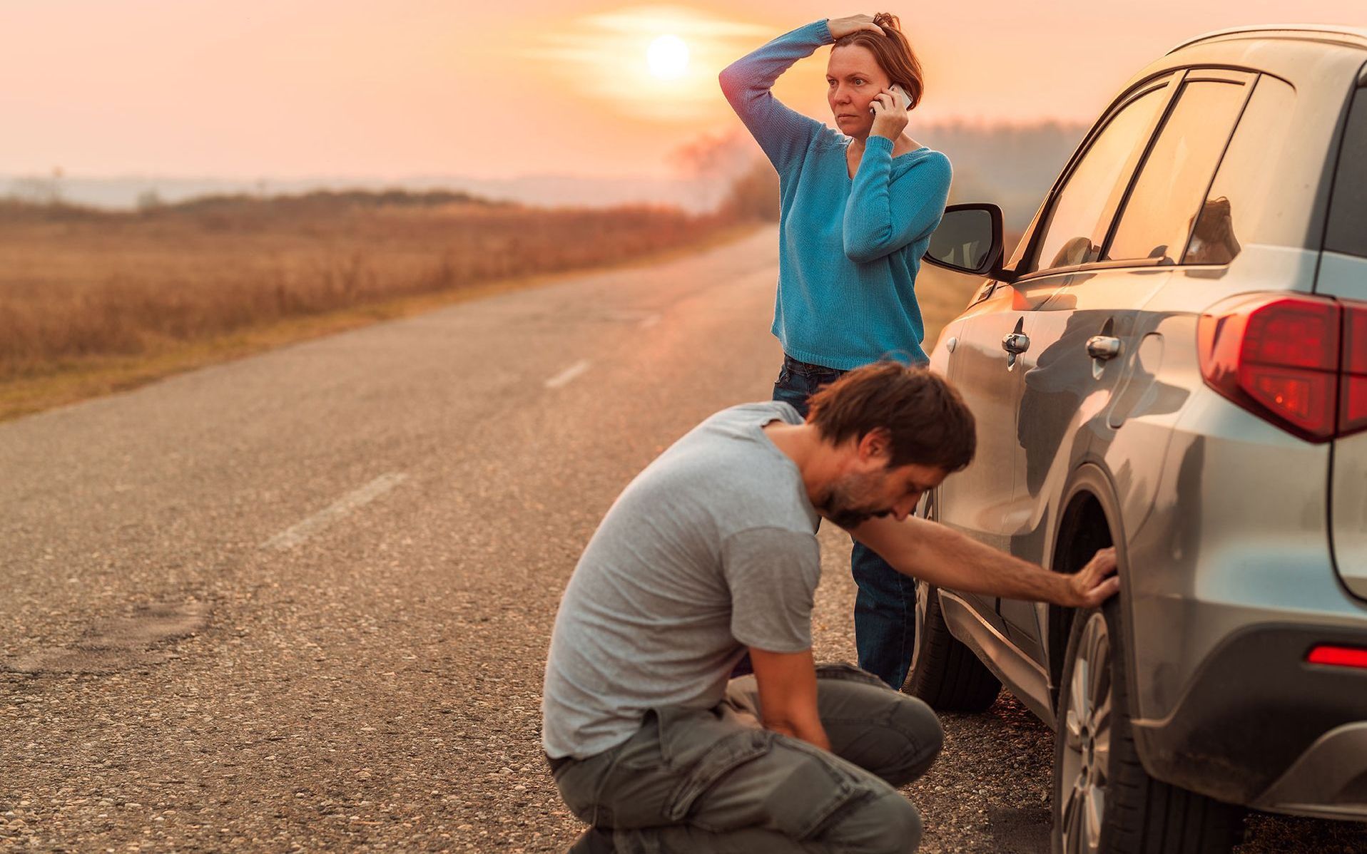 a man is changing a tire on a car while a woman talks on a cell phone .