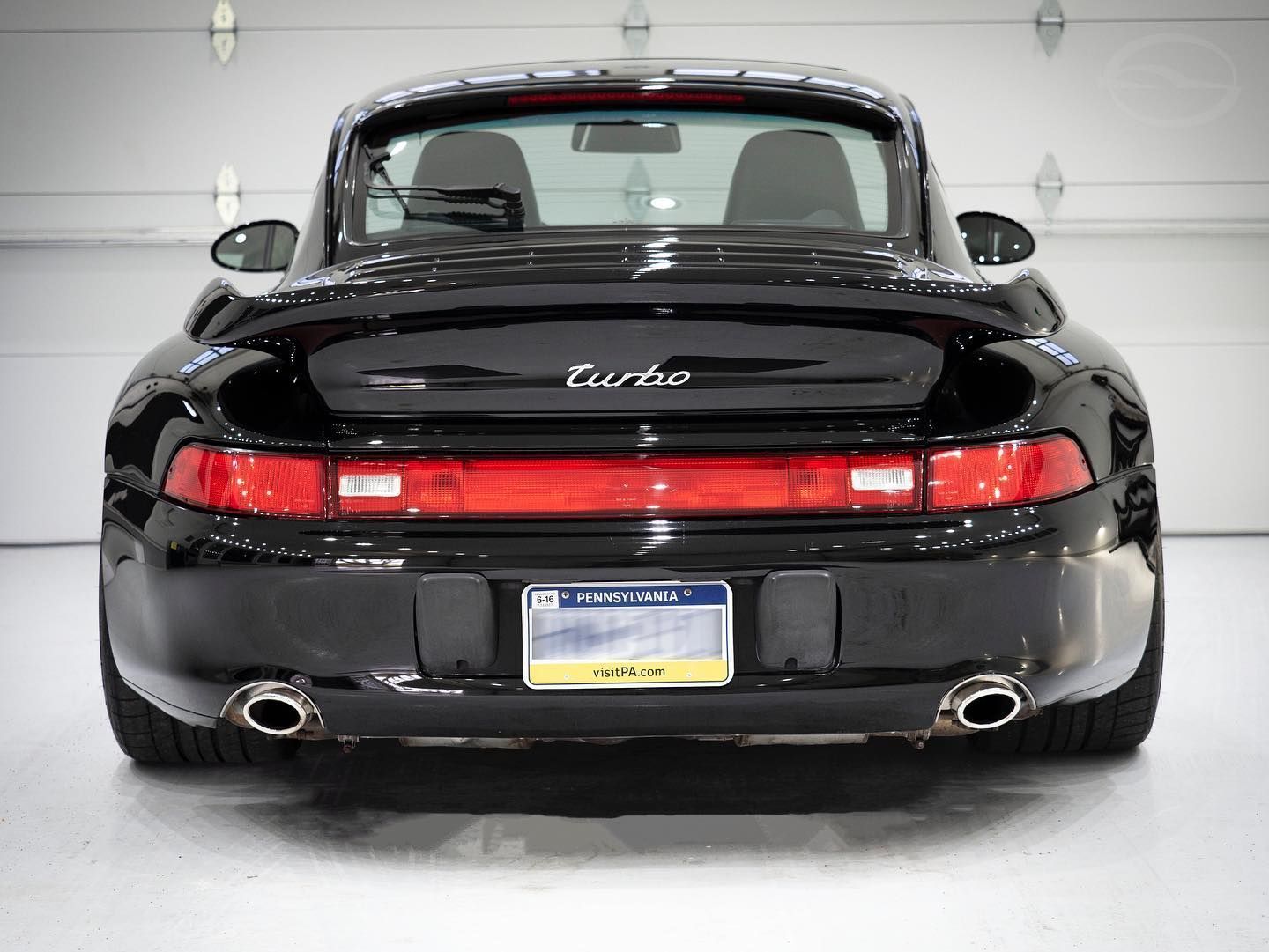A blue porsche 911 targa is parked in front of a garage door.