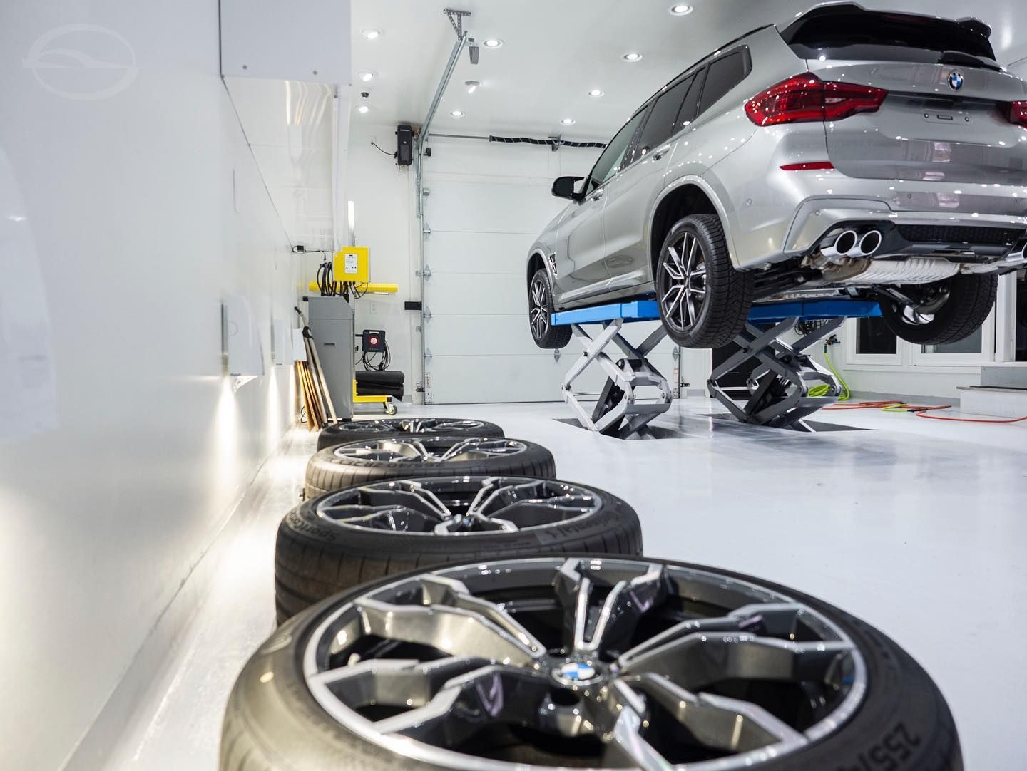 A car is sitting on a lift in a garage next to a row of tires.