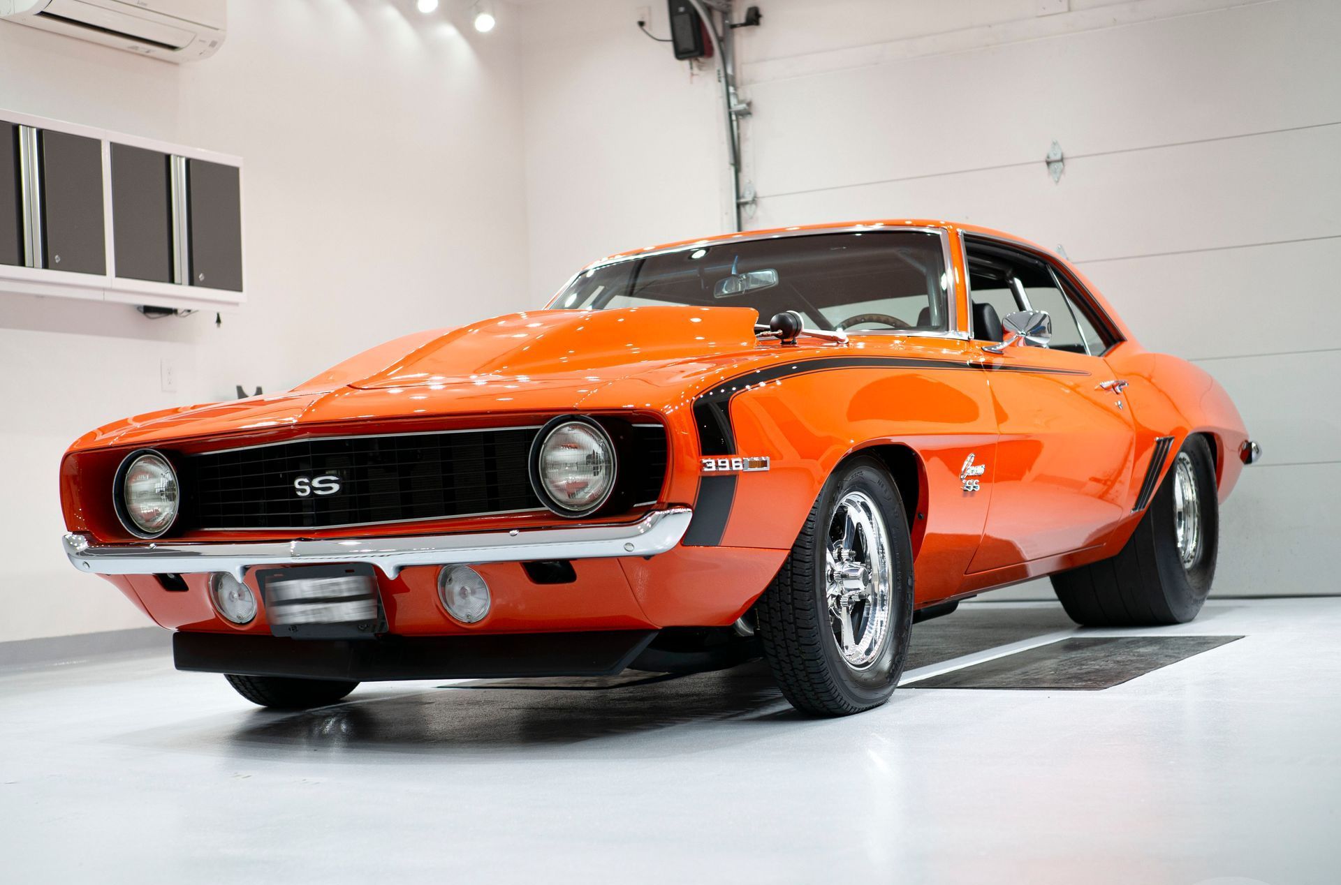 An orange chevrolet camaro is parked in a garage.