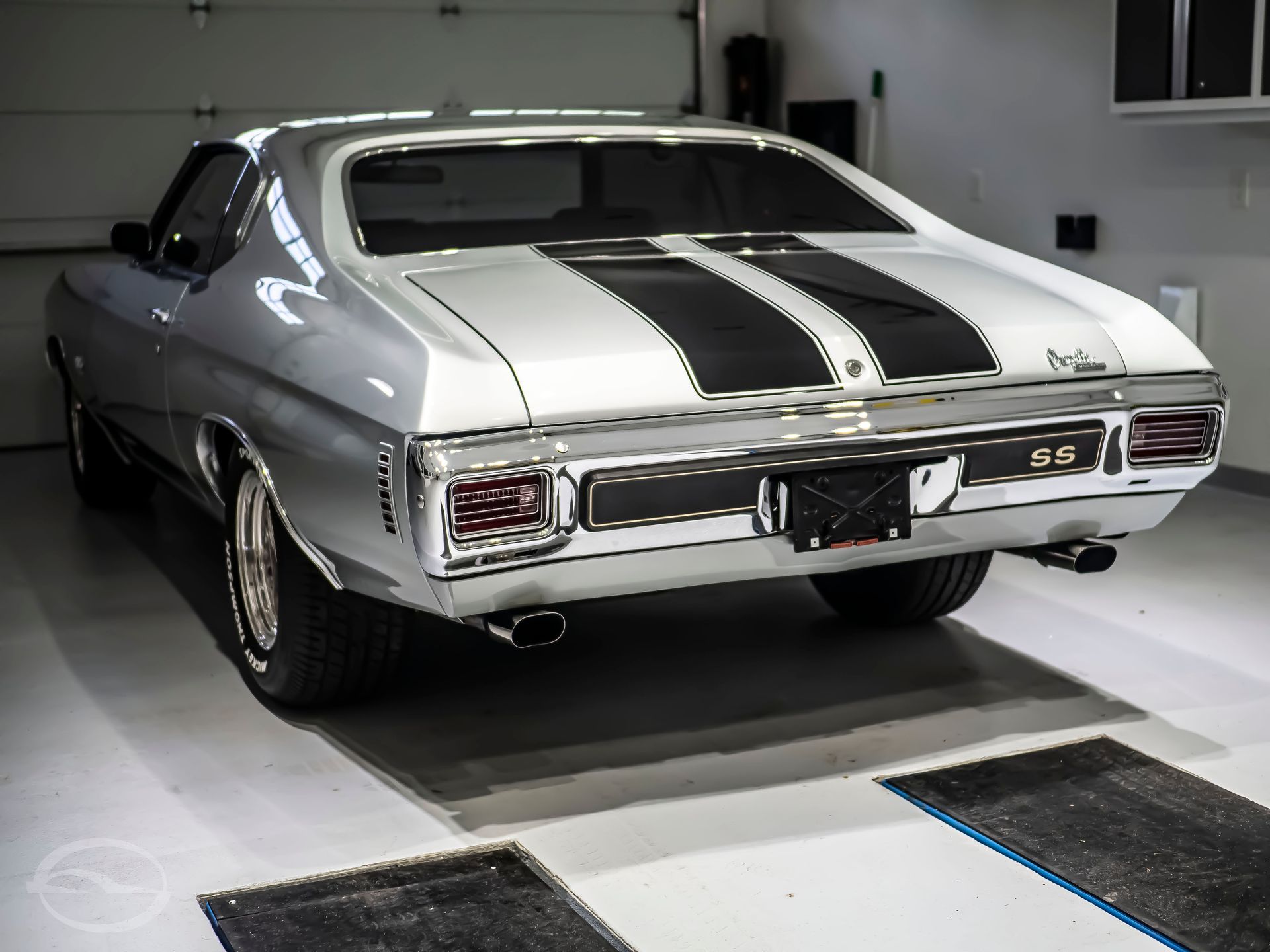 A silver car with black stripes is parked in a garage.