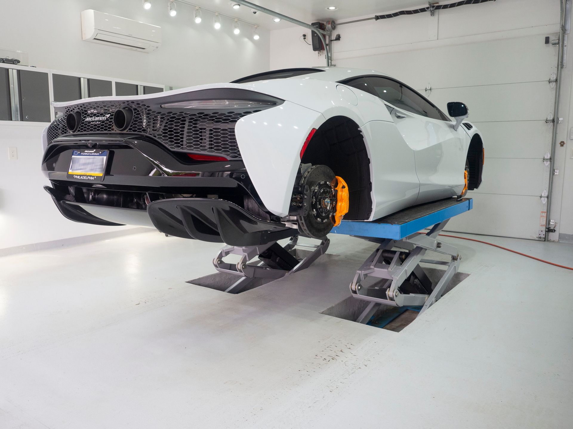 A white sports car is sitting on a lift in a garage.