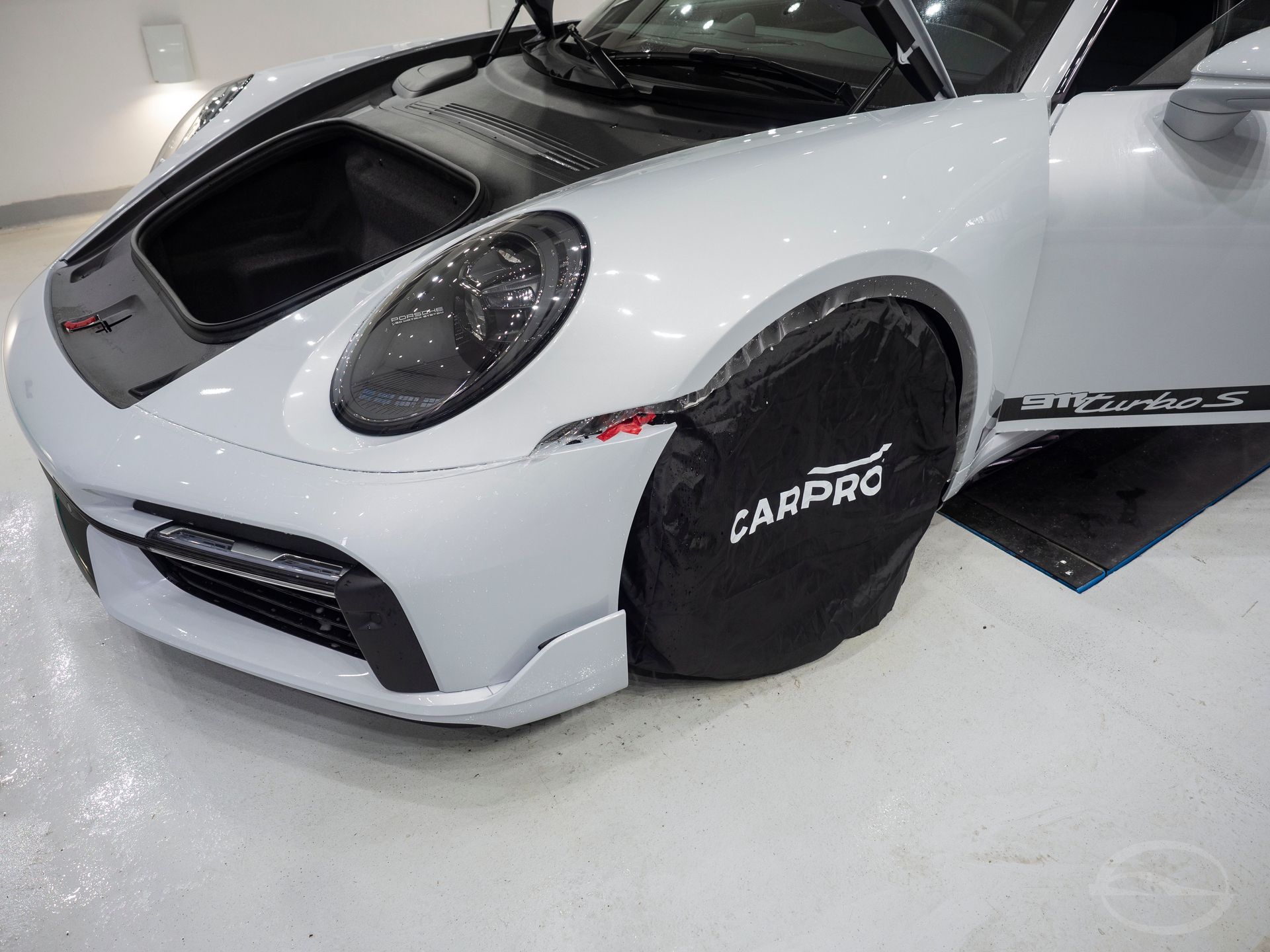 A white car with a black hood is sitting on a white floor.