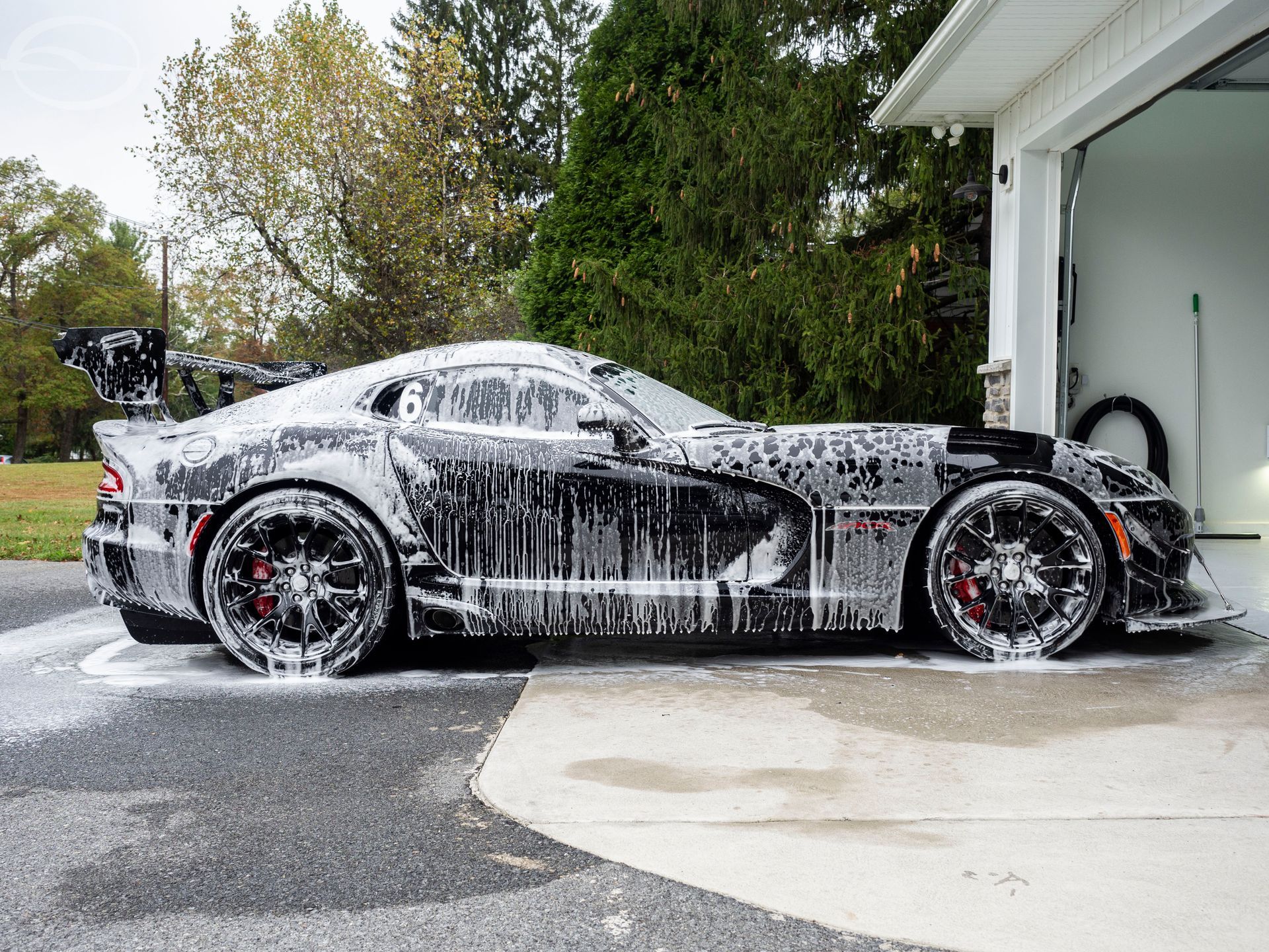 A black sports car is covered in foam in a driveway next to a garage.