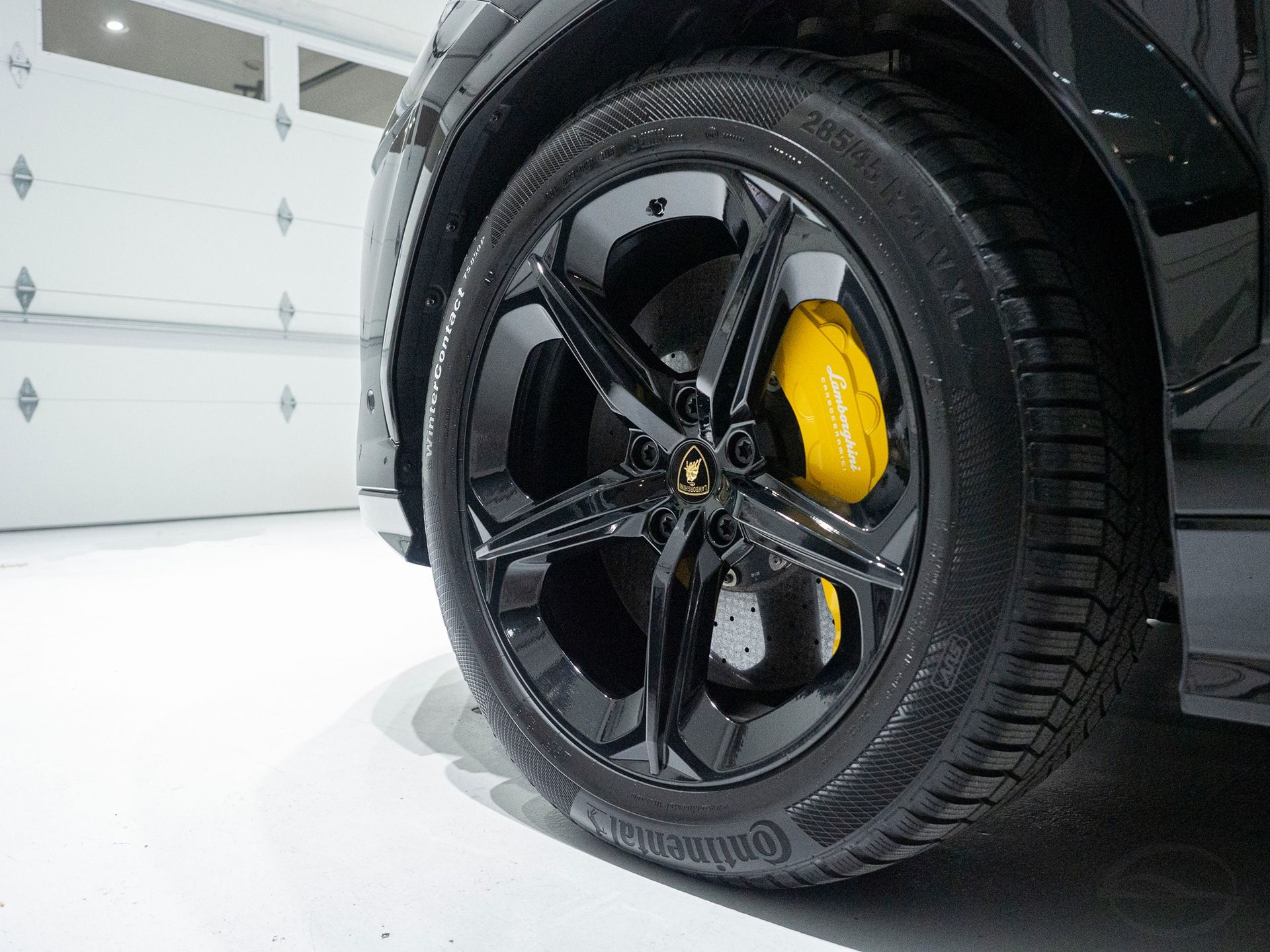 A close up of a car wheel with yellow brake calipers in a garage.