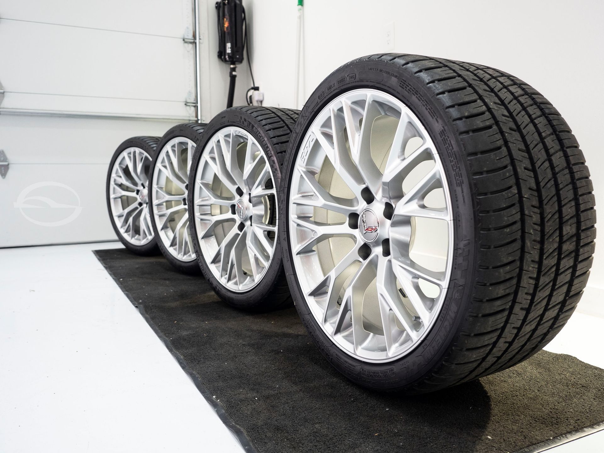 A row of tires are sitting on a mat in a garage.