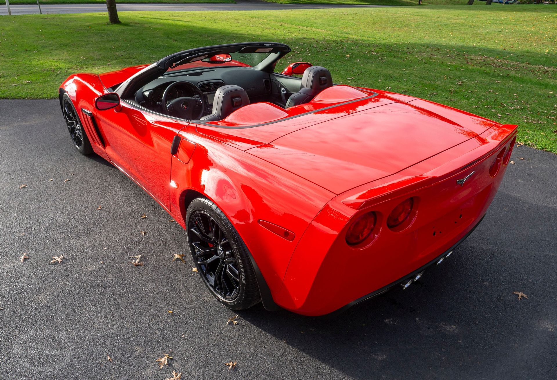 Red convertible Chevrolet Corvette parked on asphalt. Black wheels, top down, on a grassy lawn.
