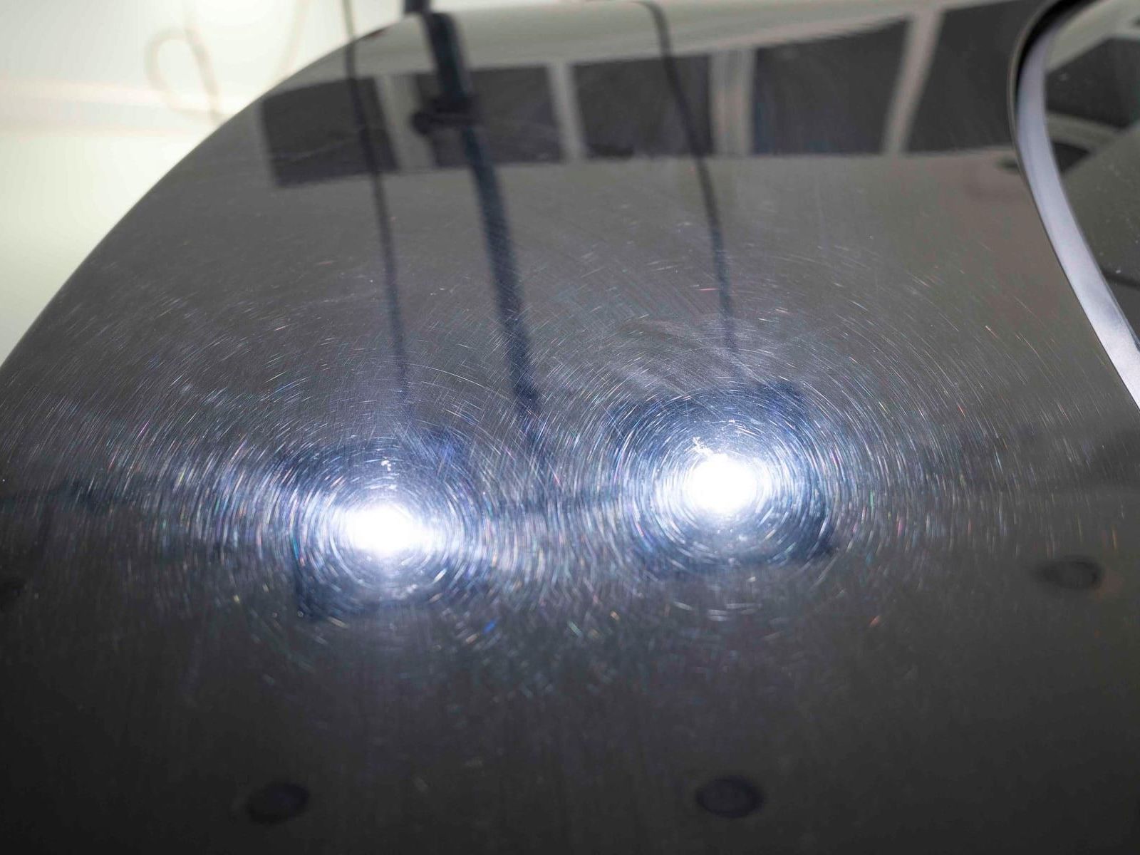Black car hood with circular swirl marks reflecting bright lights.