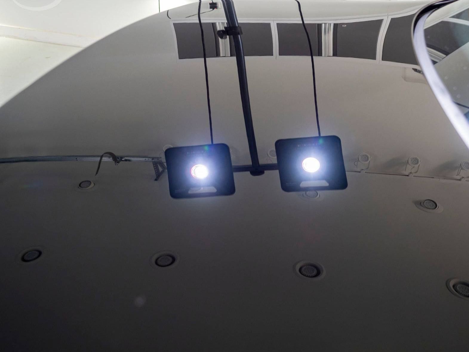 Two square, bright lights illuminate the white surface of an airplane fuselage, with a cockpit window visible on the right.