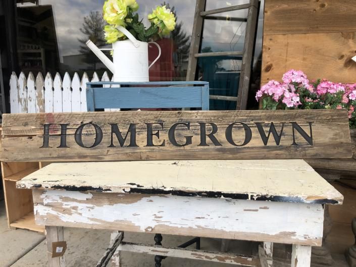 Rustic HOMEGROWN sign with white flowers and a blue box on a distressed wooden bench in front of a shop