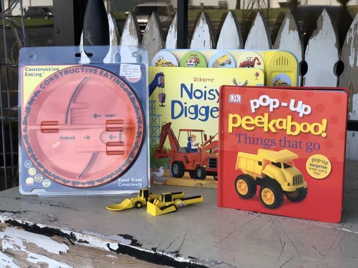 Children’s books and toy construction vehicles displayed outdoors on weathered wood.