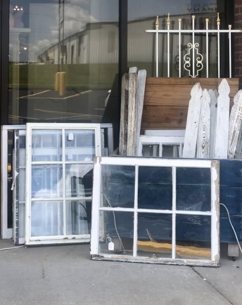 Stacked old window frames and panels leaning against a storefront exterior.
