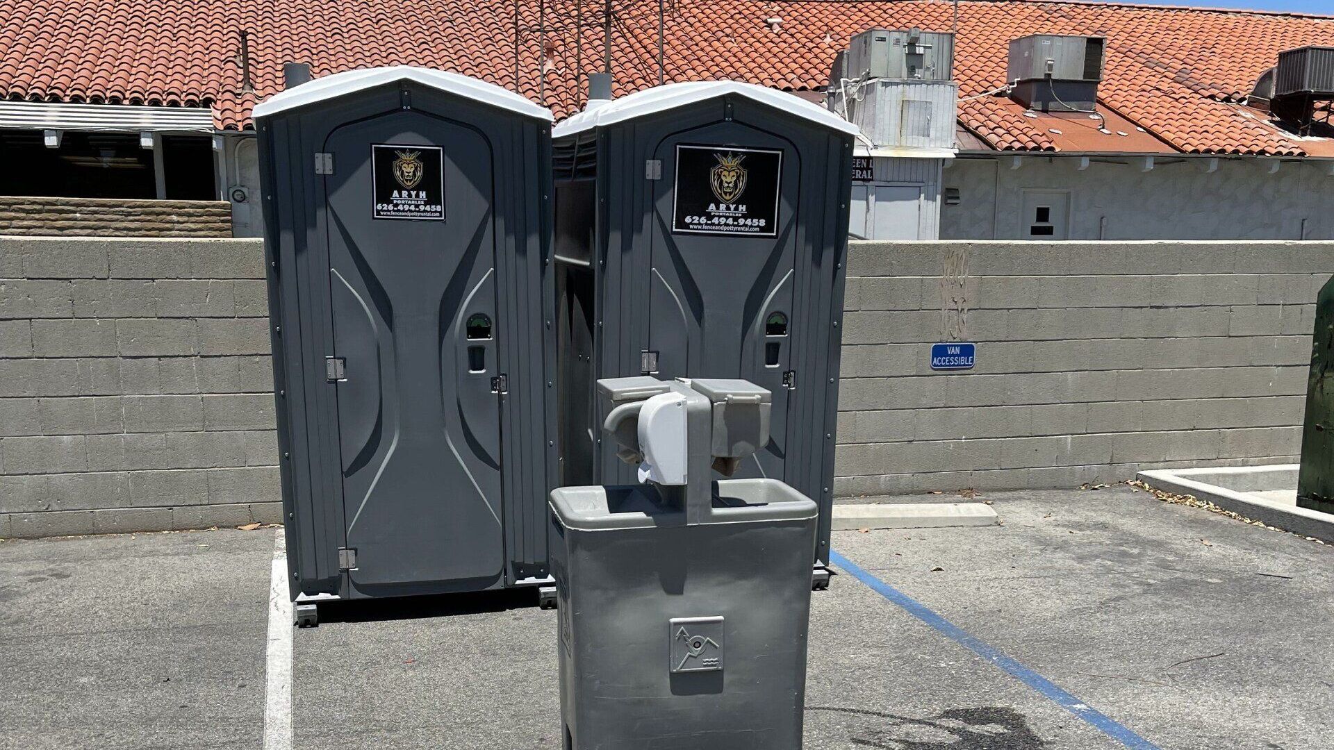 Two portable toilets and a hand washing station in a parking lot.