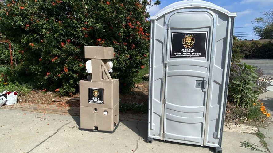 An Aryh portable toilet is next to a hand sanitizer station.