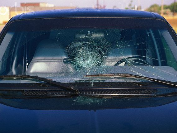 A blue car with a broken windshield is parked in a parking lot.