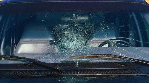 A blue car with a broken windshield is parked in a parking lot.