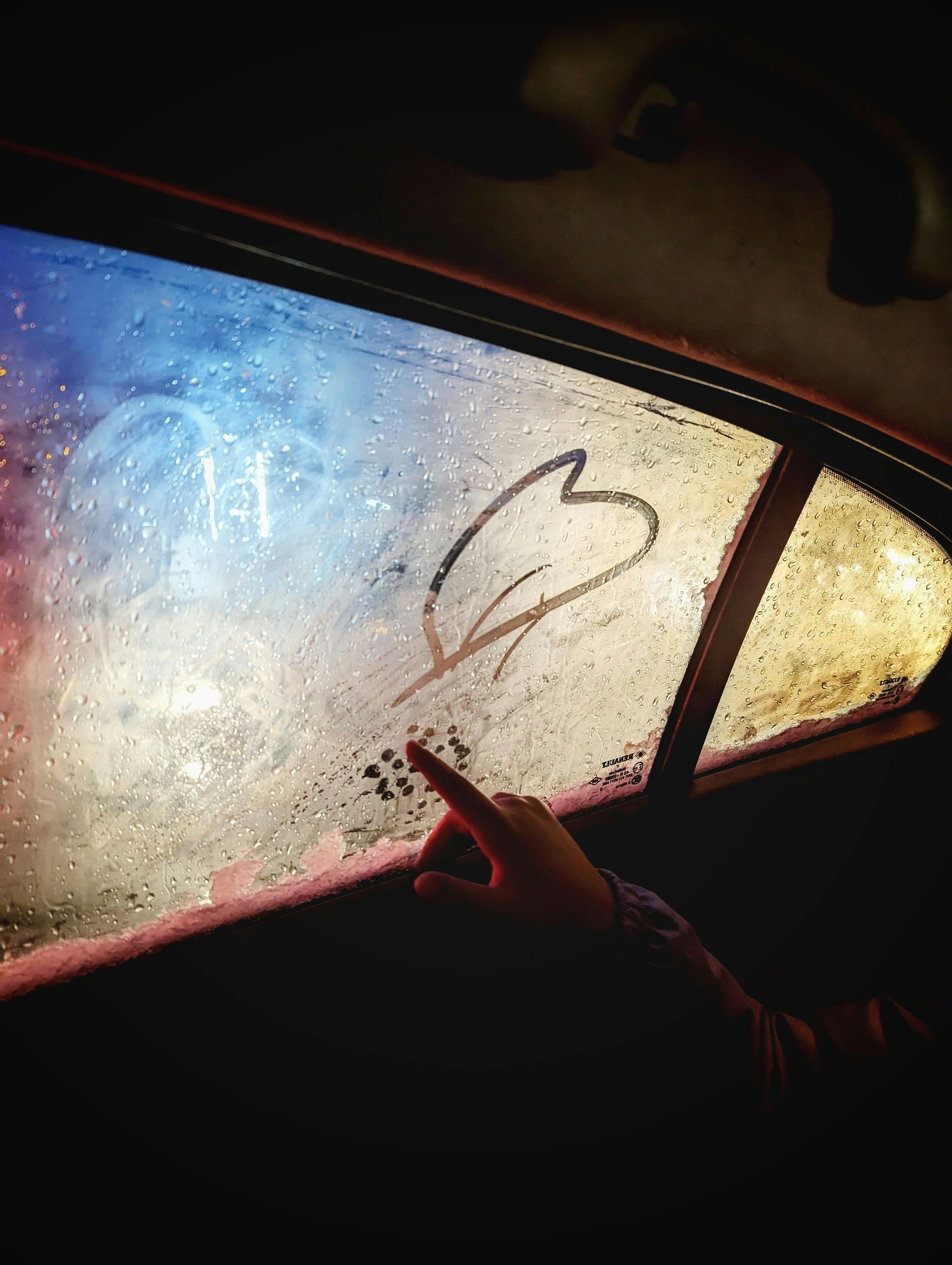 A person is pointing at a heart drawn on a car window