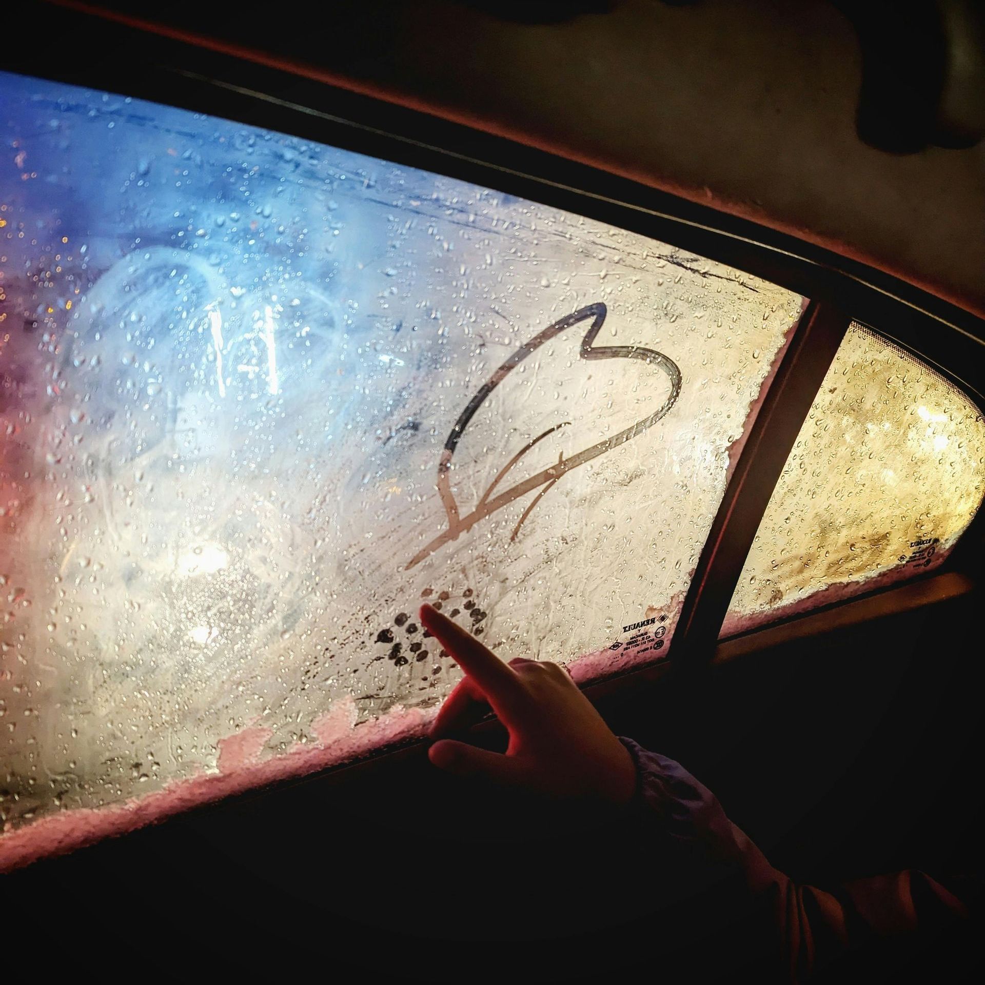 A person is pointing at a heart drawn on a car window A person is pointing at a heart drawn on a car window