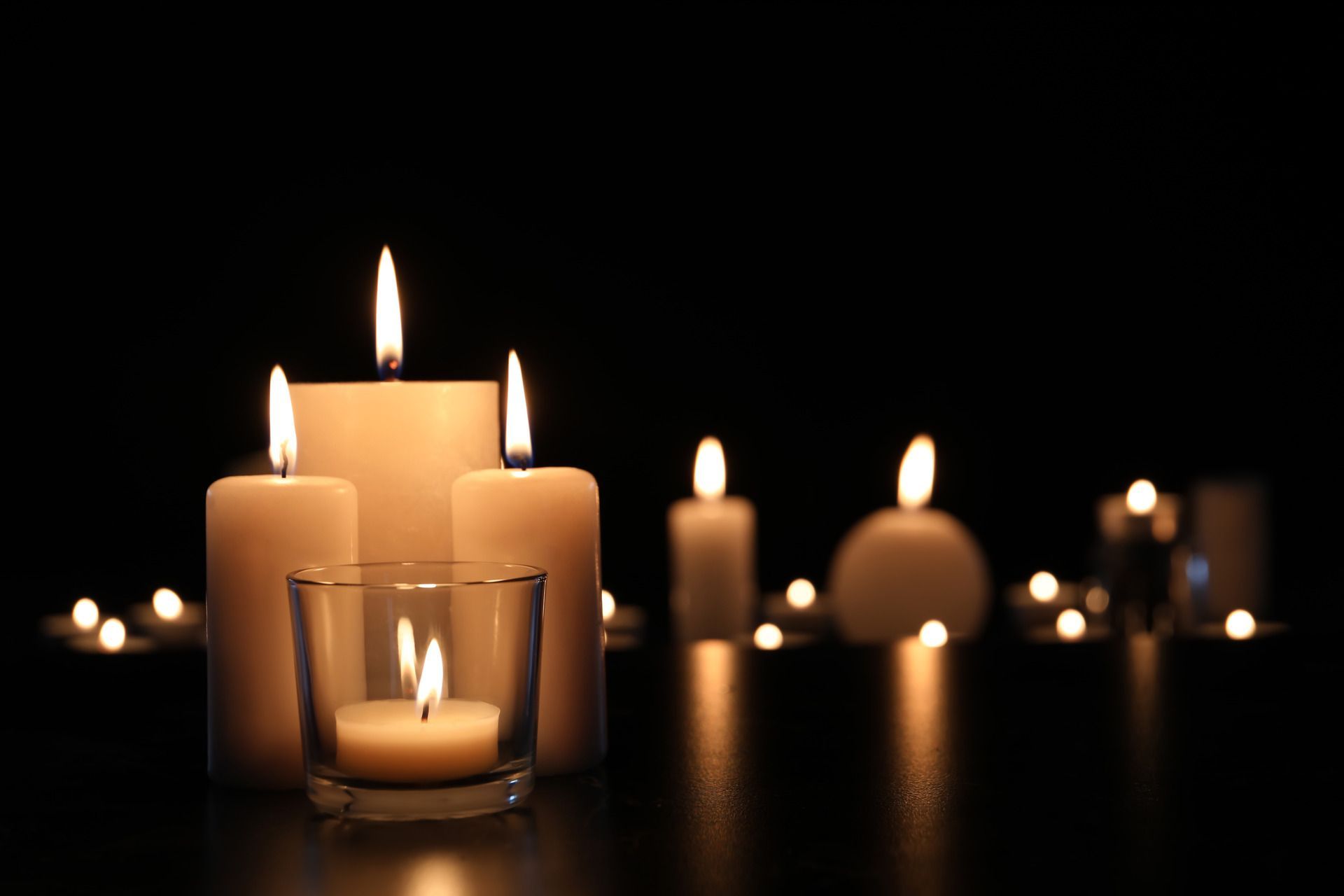Lit candles glowing in glass holders on a dark surface, creating a warm, dim atmosphere