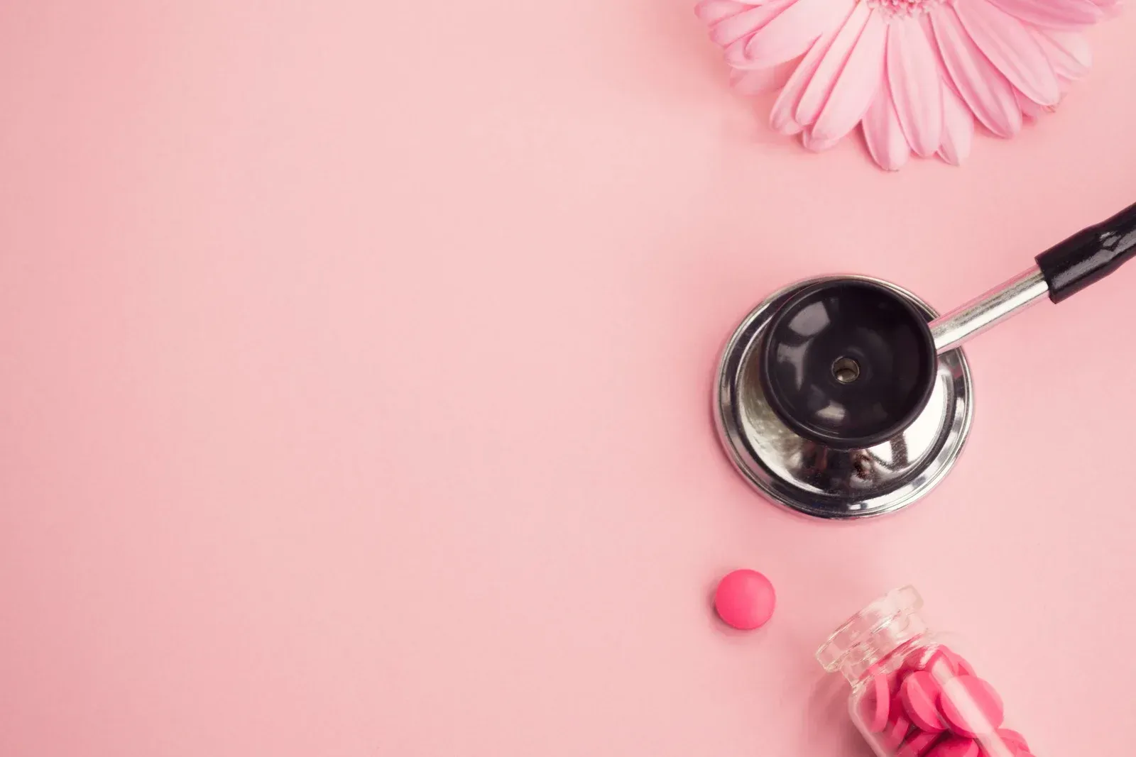A stethoscope , pills , and a pink flower on a pink background.