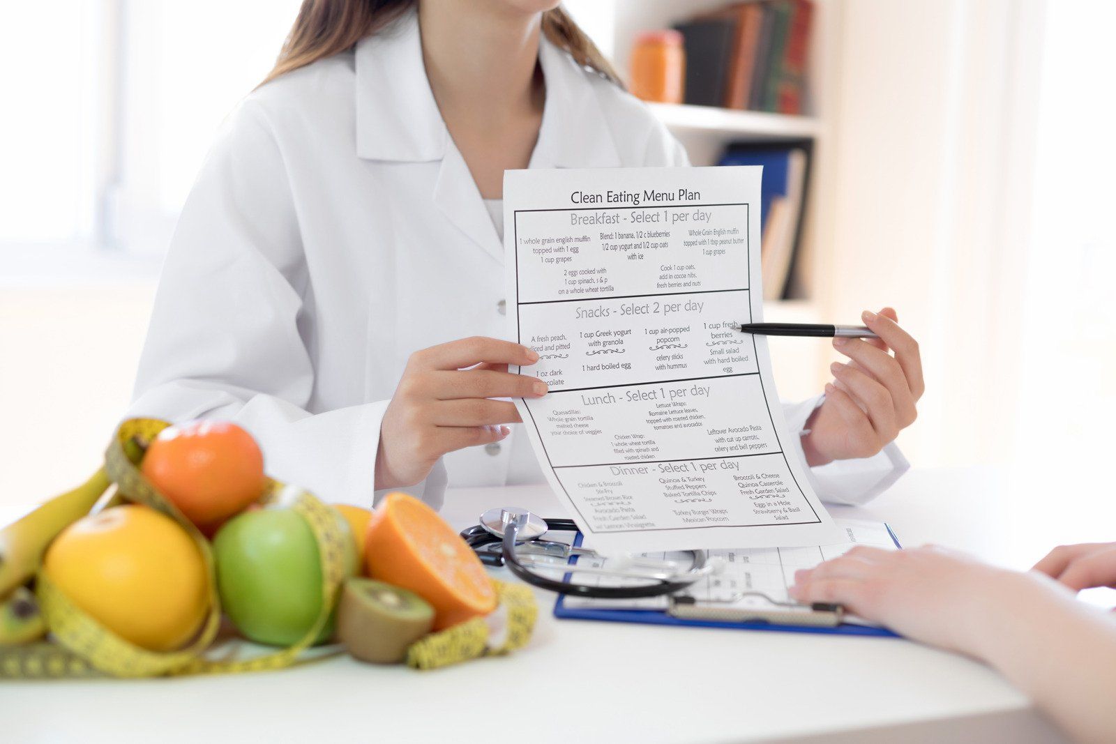 A woman is sitting at a table with fruit and holding a piece of paper.