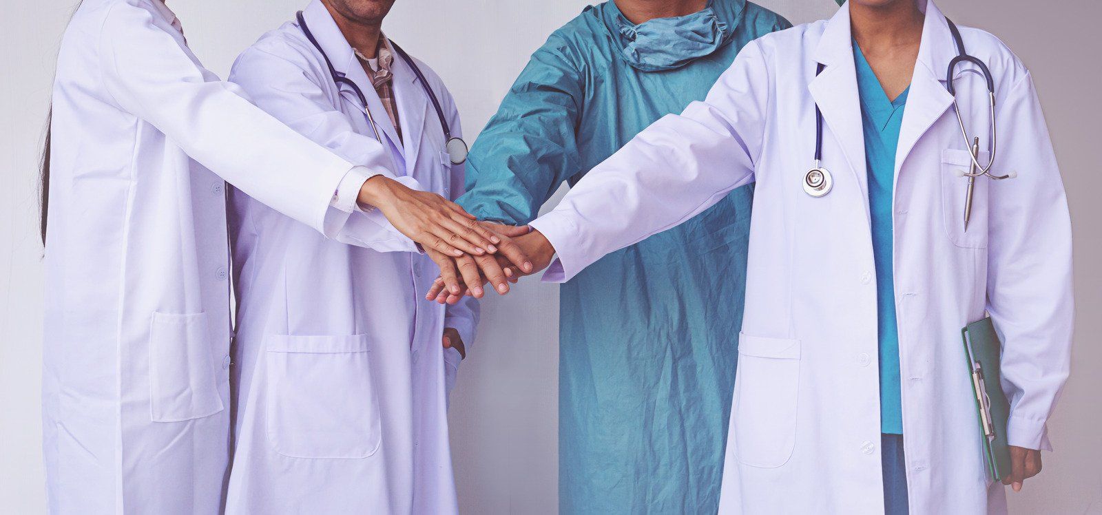 A group of doctors and nurses are putting their hands together.